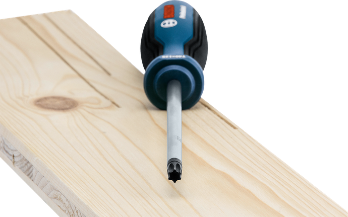 A screwdriver with a star tip rests on a light wooden plank.