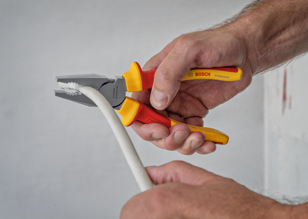 Person uses insulated pliers to grip a thick white cable.