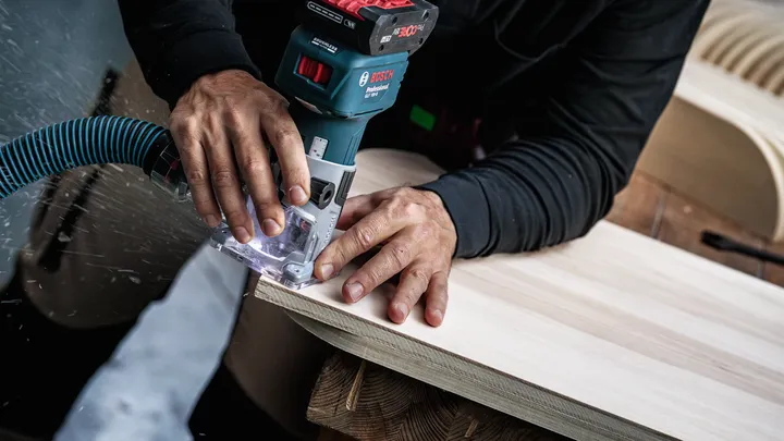 Person smooths edge of a wooden board using a cordless router.