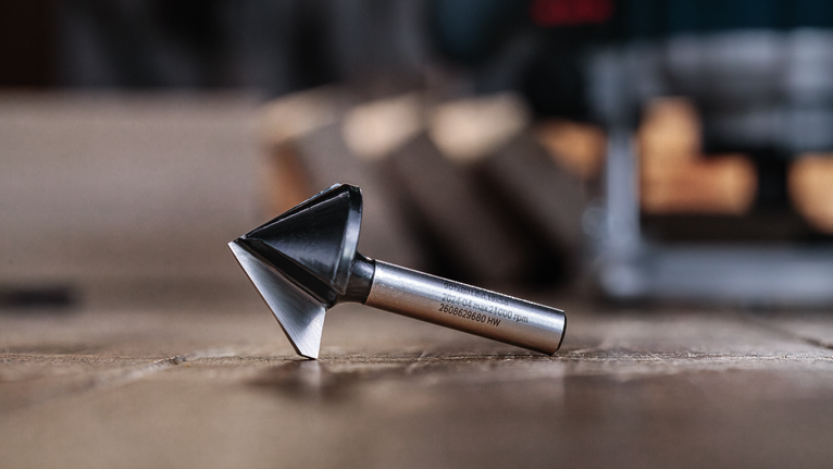 Chamfer router bit resting on a wooden surface in a workshop.