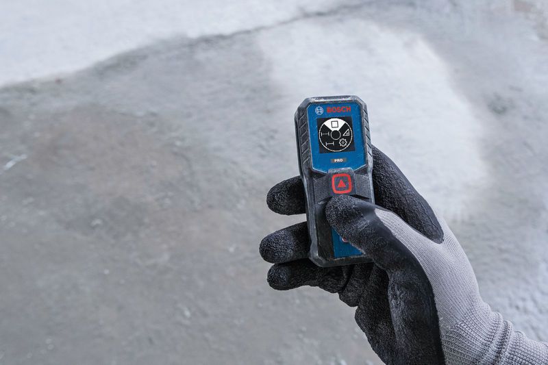 Person wearing safety equipment holding a laser measure on a concrete floor.