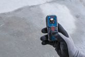 Person wearing safety equipment holding a laser measure on a concrete floor.