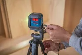 A person adjusts a laser leveling tool on a tripod indoors.