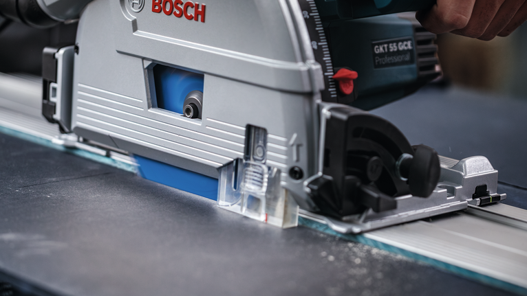 Person wearing safety equipment guides a circular saw along a straight metal rail.