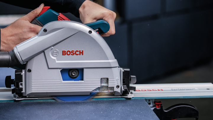 Person guides a circular saw along a track to cut a sheet of material.