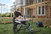 A person wearing safety equipment cuts wood with a table saw at a house construction site.