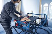 A person wearing safety equipment cuts wood on a table saw in a workshop.