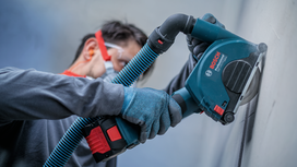 Person wearing safety equipment cuts a wall with a handheld power cutter.