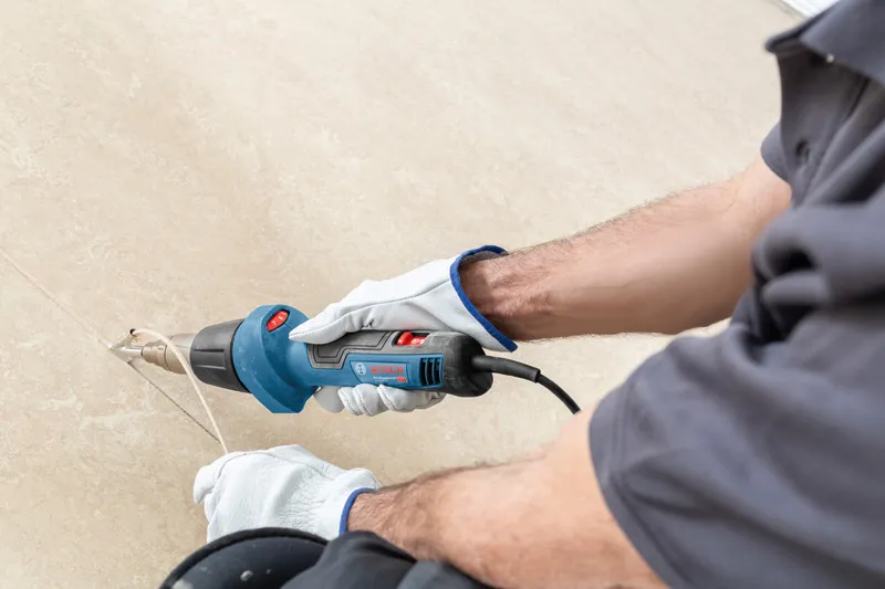 Uma pessoa que utilize equipamento de segurança utiliza uma pistola de ar quente para remover material de uma superfície.