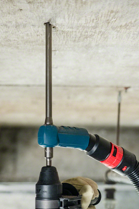 Uma pessoa que utilize equipamento de segurança perfura um teto de betão com um martelo rotativo.