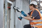 Uma pessoa que utiliza equipamento de segurança aplica vedante no batente de uma janela utilizando uma pistola de calafetagem sem fios.