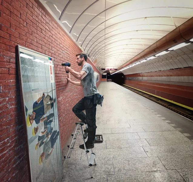 Uma pessoa que utiliza um berbequim sem fio para montar uma estrutura numa parede de tijolos numa estação de metro.