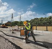 Uma pessoa que utiliza equipamento de segurança utiliza uma serra alternativa para cortar um cano num estaleiro de obras.