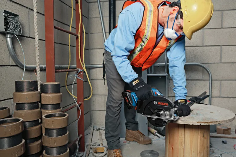 Uma pessoa que utiliza equipamento de segurança corta madeira com uma serra manual num estaleiro de construção.