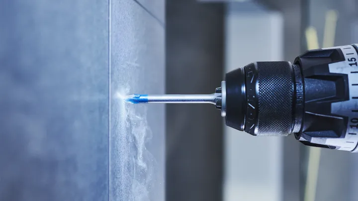 Um berbequim elétrico a fazer um furo numa parede de azulejos.