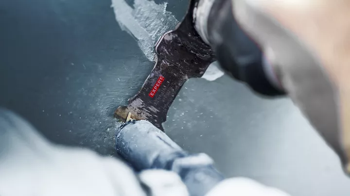 Pessoa a cortar um cano de metal pintado com uma lâmina de serra alternativa.