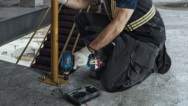 Uma pessoa que usa equipamento de segurança aperta um parafuso num poste de metal usando uma chave de impacto sem fios.