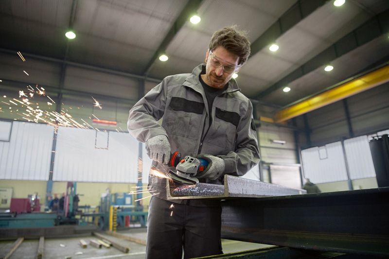 Uma pessoa que usa equipamento de segurança tritura uma viga de aço, produzindo faíscas.