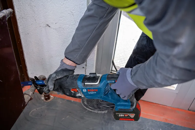 Uma pessoa que utiliza equipamento de segurança utiliza uma serra alternativa para cortar metal perto de um batente de porta.