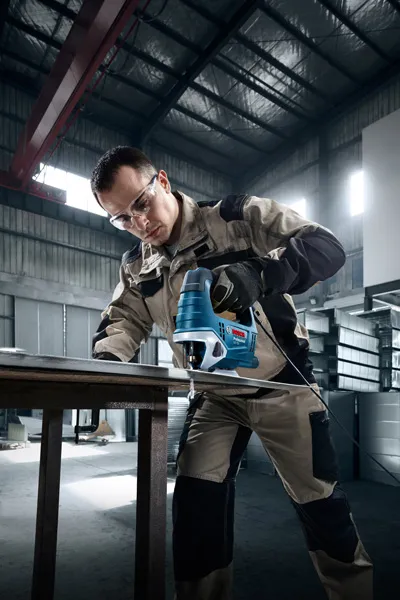 Uma pessoa que usa equipamento de segurança utiliza uma serra de tico-tico para cortar metal numa oficina.