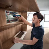 Uma pessoa prende fios a um painel elétrico usando uma chave de fendas sem fios.