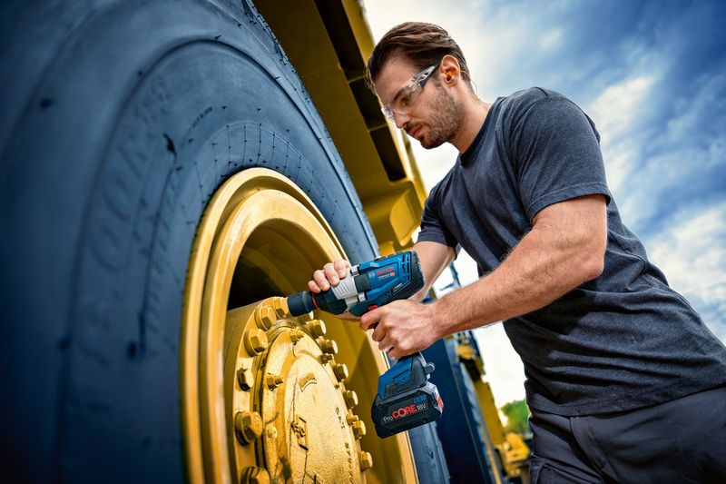 Uma pessoa que utiliza equipamento de segurança utiliza uma chave de impacto numa roda grande de um veículo.