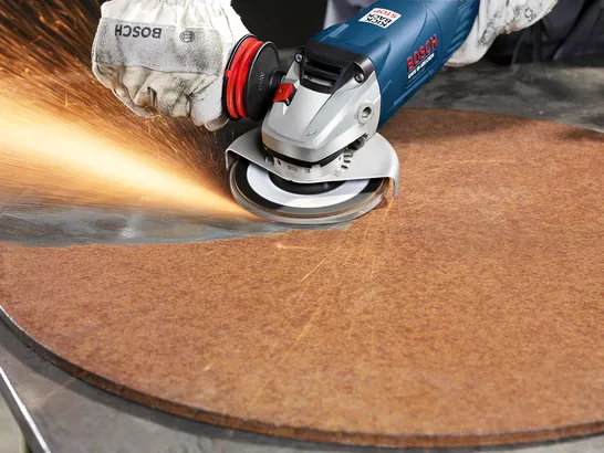 Uma pessoa que usa equipamento de segurança tritura a borda de uma folha circular, produzindo faíscas.