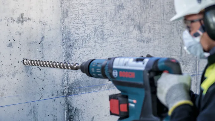 Uma pessoa que utilize equipamento de segurança perfura uma parede de betão.