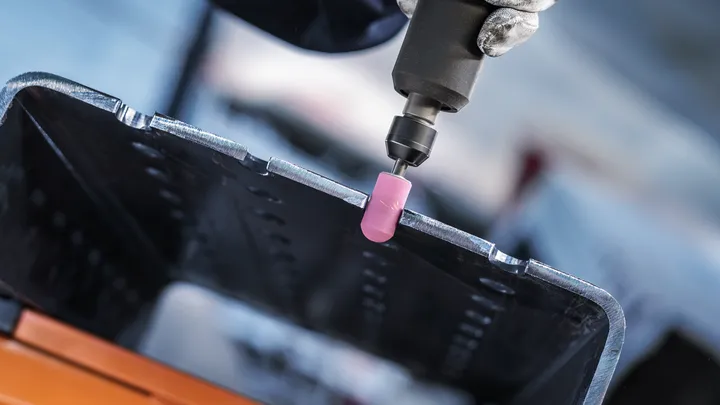 Uma pessoa que usa equipamento de segurança utiliza uma ferramenta elétrica com um acessório de retificação cor-de-rosa em metal.