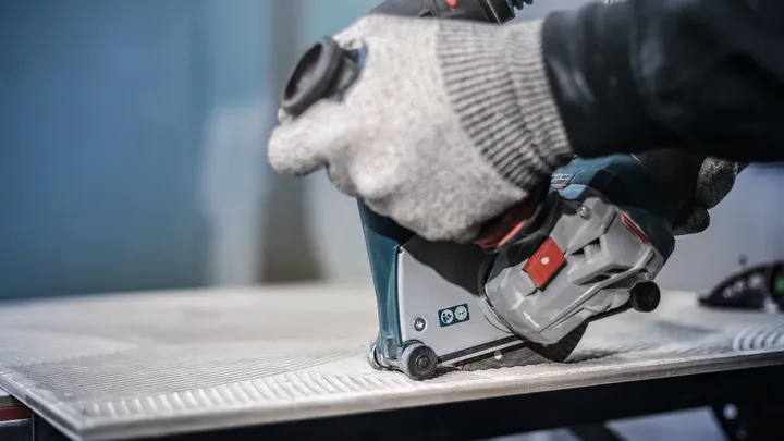 Uma pessoa que usa equipamento de segurança utiliza uma ferramenta elétrica para cortar um azulejo.