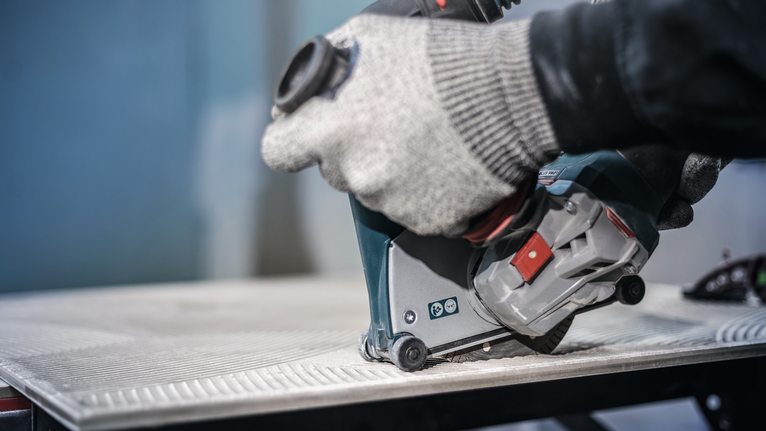 Uma pessoa que usa equipamento de segurança utiliza uma ferramenta elétrica para cortar um azulejo.