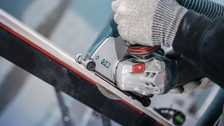 Uma pessoa que usa equipamento de segurança utiliza uma ferramenta elétrica para cortar uma barra de metal.