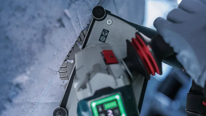 Uma pessoa que utilize equipamento de segurança perfura uma parede de betão com uma ferramenta elétrica.