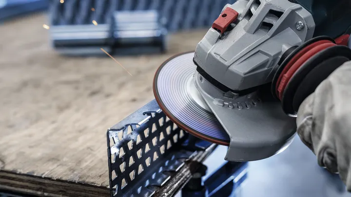 Uma pessoa que utilize equipamento de segurança retifica uma viga metálica com uma rebarbadora.