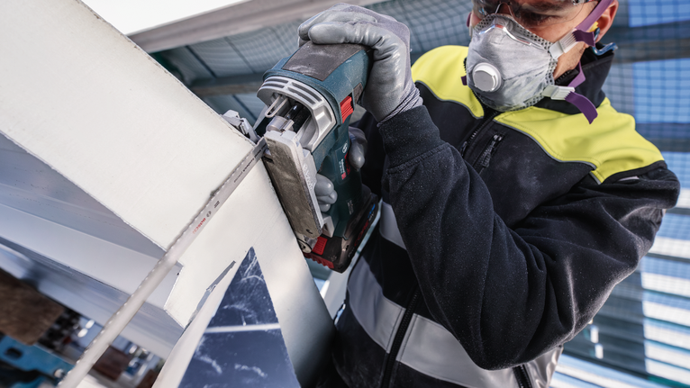 Uma pessoa que usa equipamento de segurança corta uma viga metálica com uma ferramenta elétrica.