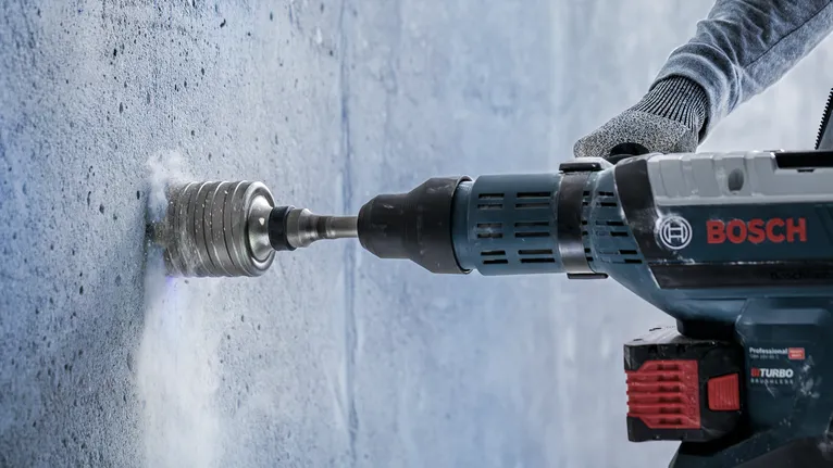 Pessoa que usa equipamento de segurança faz um furo numa parede de betão.