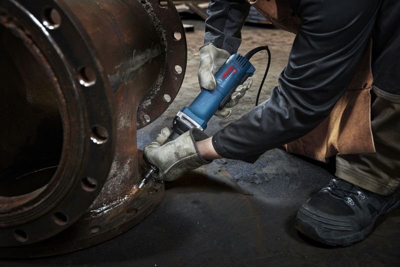 Uma pessoa que usa equipamento de segurança utiliza uma retificadora reta numa flange de metal.