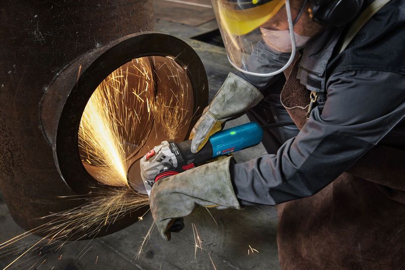 Uma pessoa que usa equipamento de segurança tritura um grande cano de metal, criando faíscas brilhantes.