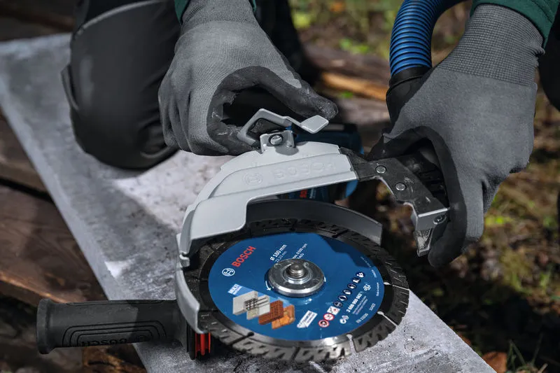 Uma pessoa que utilize equipamento de segurança liga uma proteção de extração de pó a uma rebarbadora de grandes dimensões.