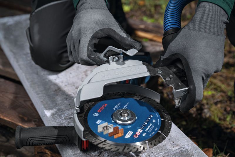 Uma pessoa que utilize equipamento de segurança liga uma proteção de extração de pó a uma rebarbadora de grandes dimensões.