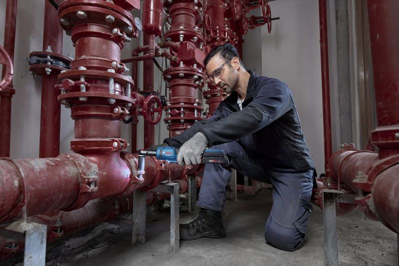 Uma pessoa que utiliza equipamento de segurança utiliza uma chave de roquete sem fios num sistema de tubagem vermelha.