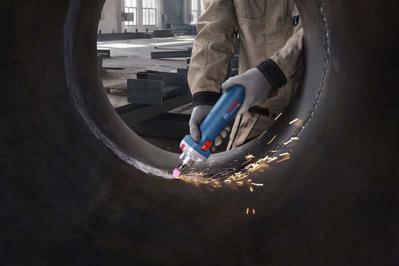 Uma pessoa que usa equipamento de segurança tritura o interior de um grande tubo de metal com uma retificadora reta.