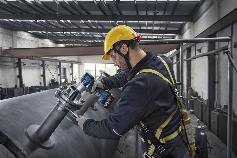 Uma pessoa que usa equipamento de segurança utiliza uma chave de impacto para apertar parafusos num grande tanque de metal.