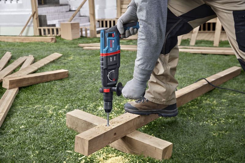 Uma pessoa que utiliza equipamento de segurança perfura uma viga de madeira num estaleiro de obras.