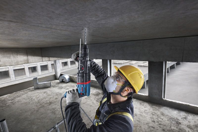 Uma pessoa que utiliza equipamento de segurança perfura um teto de betão num estaleiro de obras.