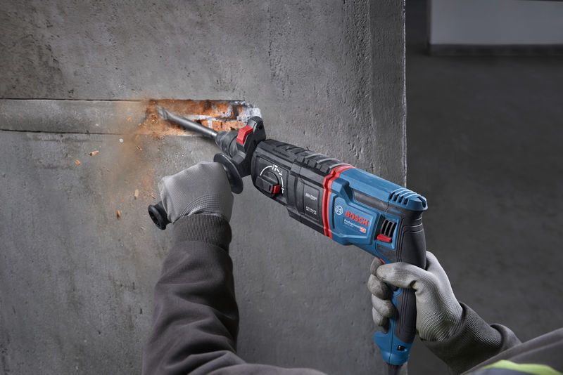Uma pessoa que usa equipamento de segurança utiliza um martelo rotativo para fazer uma ranhura no betão.