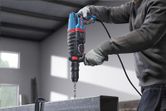 Uma pessoa que utilize equipamento de segurança perfura uma viga metálica utilizando um martelo rotativo.