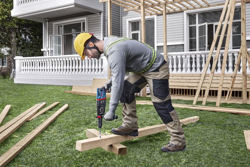 Uma pessoa que utiliza equipamento de segurança perfura vigas de madeira num estaleiro de obras.