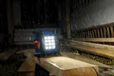 Luz de trabalho sem fios a iluminar tábuas de madeira sob chuva forte num estaleiro de obras.