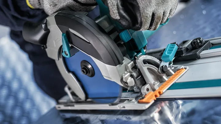 Uma pessoa que utilize equipamento de segurança opera uma serra circular num carril-guia.